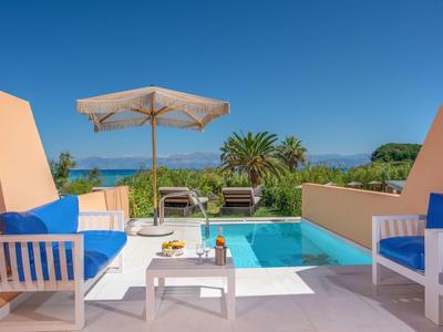 Outdoor seating area with blue cushions by a pool under a clear sky, surrounded by greenery.