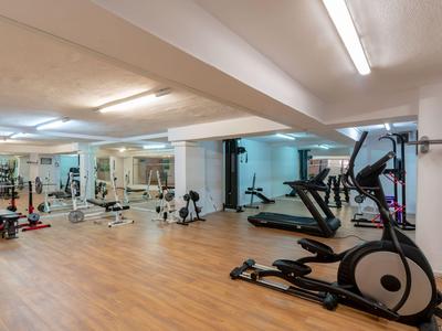 Moderner Fitnessraum mit verschiedenen Trainingsgeräten und Spiegeln an den Wänden.