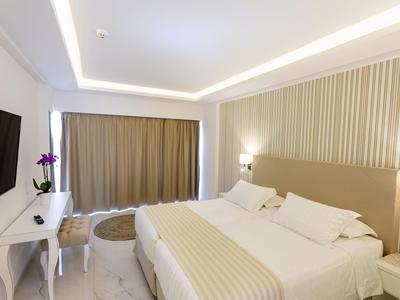 Bright hotel room with beige decor, large bed, TV, desk, and closed curtains.