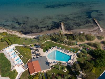 Aerial view of a coastal hotel with a blue swimming pool and sunbeds near the sea shore.