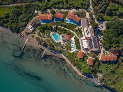 Aerial view of a coastal resort with multiple buildings, pools, and green landscaping near clear water.