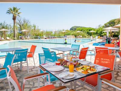 Outdoor dining area with colorful chairs by a sunny pool surrounded by greenery.