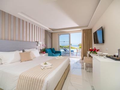 Bright hotel room with king bed, balcony view, blue armchair, and modern decor.