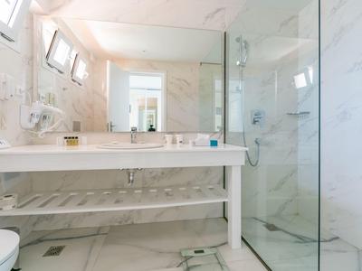 Bright modern bathroom with marble walls, glass shower, and white vanity with large mirror.