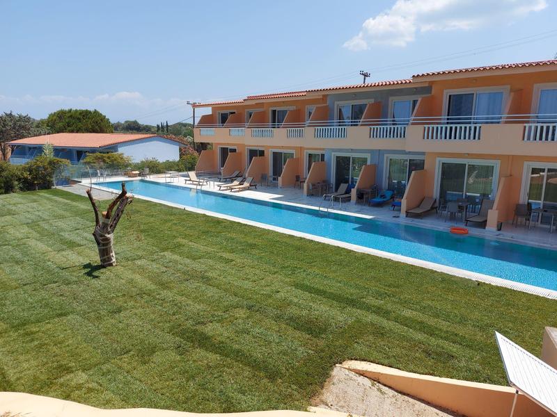 Hotel with pool, sun loungers, lawn, and clear blue sky.