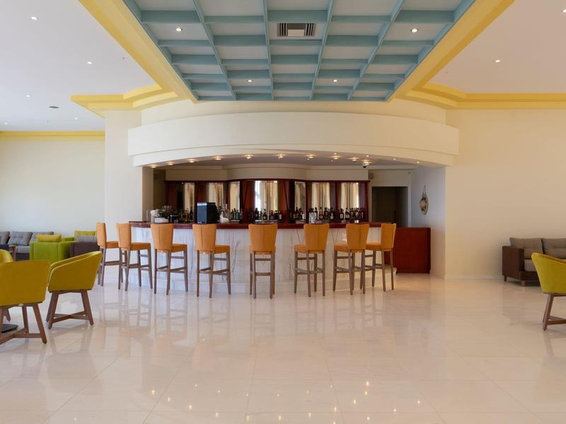 Spacious hotel lobby with bar, high stools, and colorful lounge chairs on shiny floor.