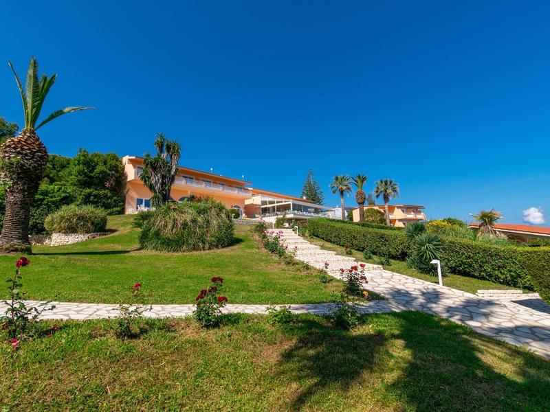 Sunny hotel with palm trees and a green lawn under a clear blue sky.