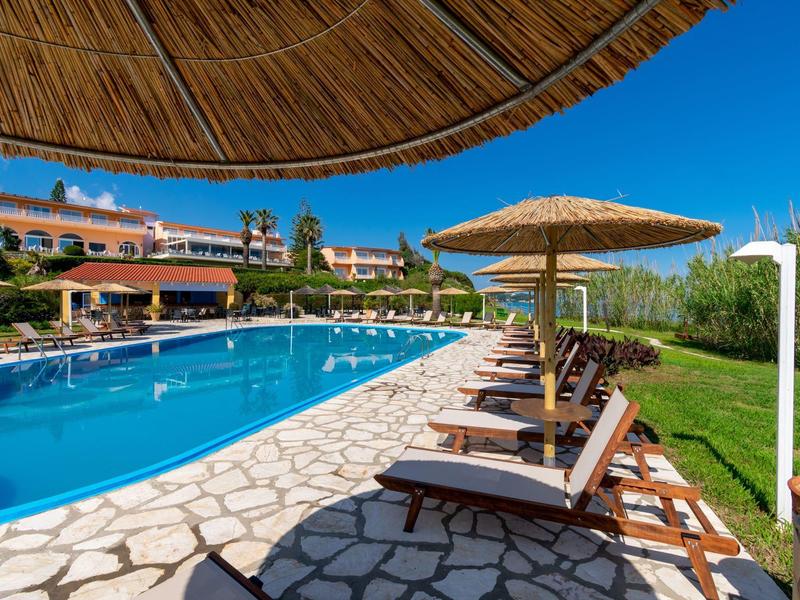 Sun loungers under straw umbrellas by a pool with clear blue sky at a resort.