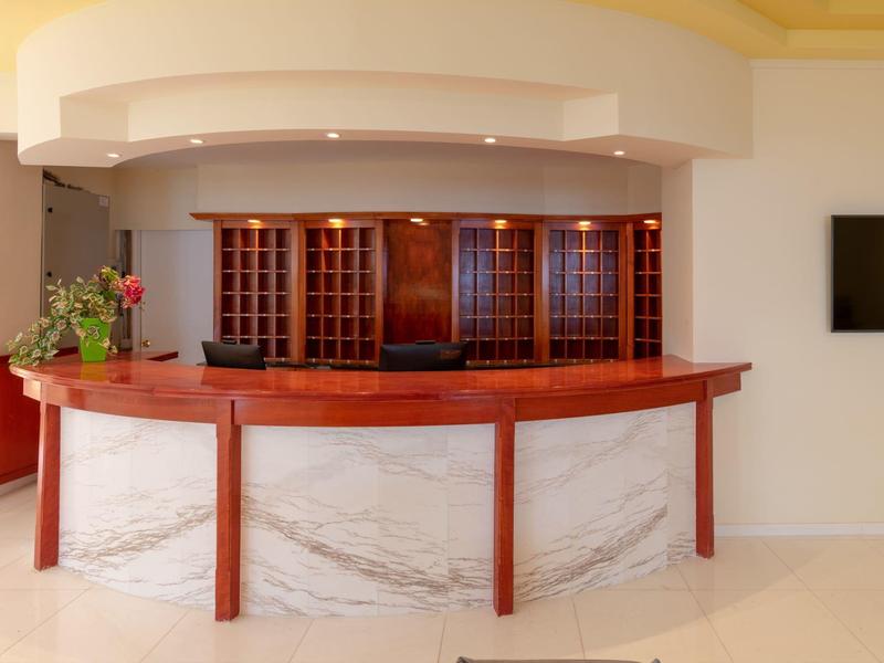 Hotel reception desk with wooden countertop, flower arrangement, and TV on the wall.