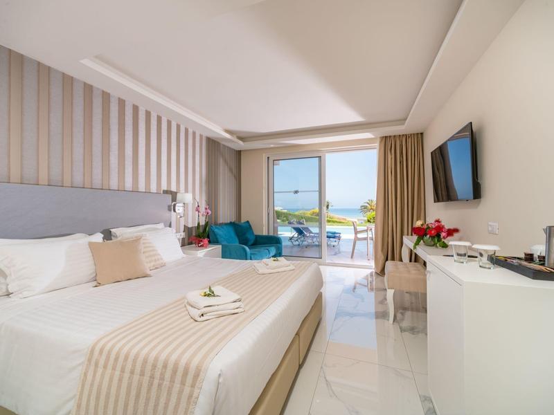 Bright hotel room with king bed, balcony view, blue armchair, and modern decor.