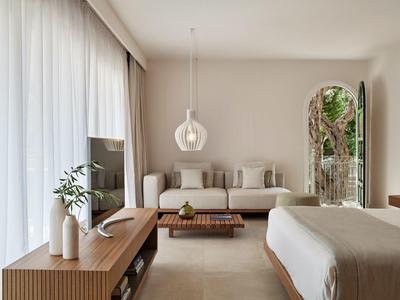 Helles, modernes Schlafzimmer mit großem Bett, Sofa, TV, Holzkommode und bodentiefen Vorhängen.