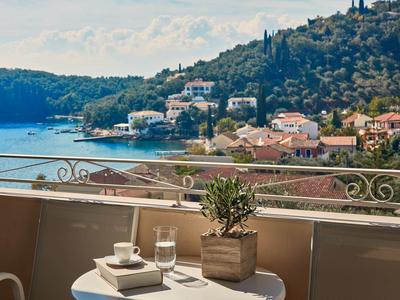 Balkon mit Tisch, Tasse, Buch, Pflanze und Blick auf Küste mit Häusern und grünen Hügeln.