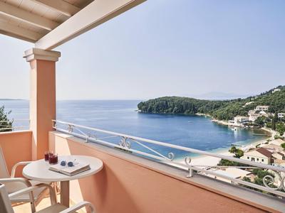 Balkon mit Tisch, zwei Stühlen und Meeresblick auf Küste und bewaldete Hügel.