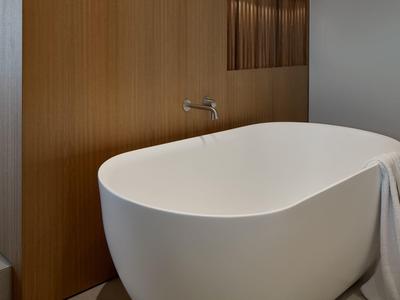 Moderne weiße freistehende Badewanne vor Holzpaneel mit Wandarmatur und Handtuch.