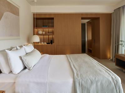 Hell eingerichtetes Schlafzimmer mit großem Bett, Holzschrank und Fenster mit weißen Vorhängen.