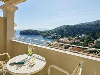 Balkon mit Tisch und Stühlen, Blick auf das Meer und grüne Hügel mit Häusern.
