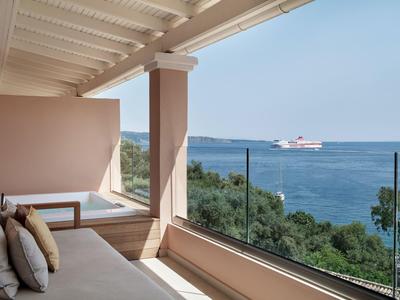 Hotelový balkon s pohovkou, skleněným zábradlím a výhledem na moře a projíždějící trajekt.