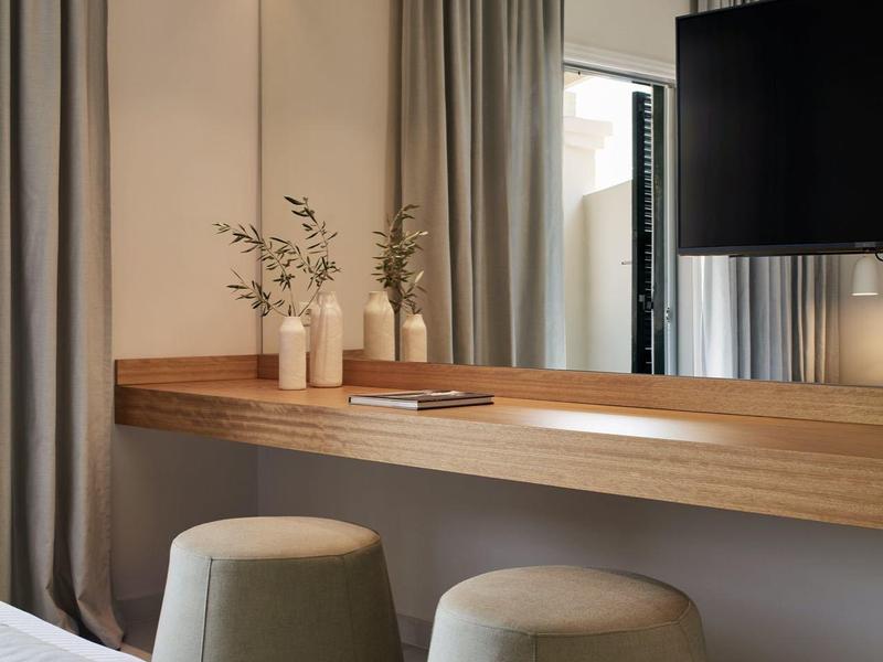 Schlichte Schlafzimmer-Ecke mit grauen Vorhängen, zwei grauen Hockern und Holzablage mit Vasen.