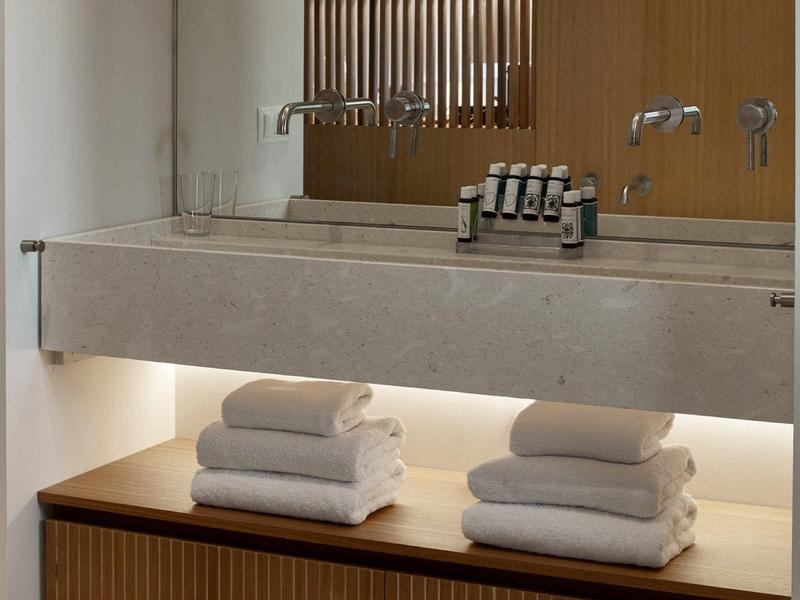 Minimalistisches Badezimmer mit Betonwaschbecken, Holzschrank und weißen, gefalteten Handtüchern.