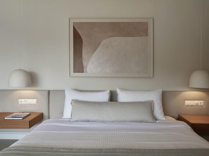 Modernes Schlafzimmer mit großem Bett, neutralen Farben, Wandbild und zwei Nachttischen mit Lampen.