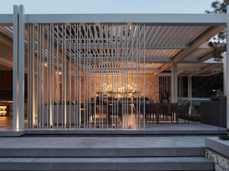 Moderner, offener Pavillon mit weißen Stäben, Glaswänden und eleganter Beleuchtung bei Dämmerung.