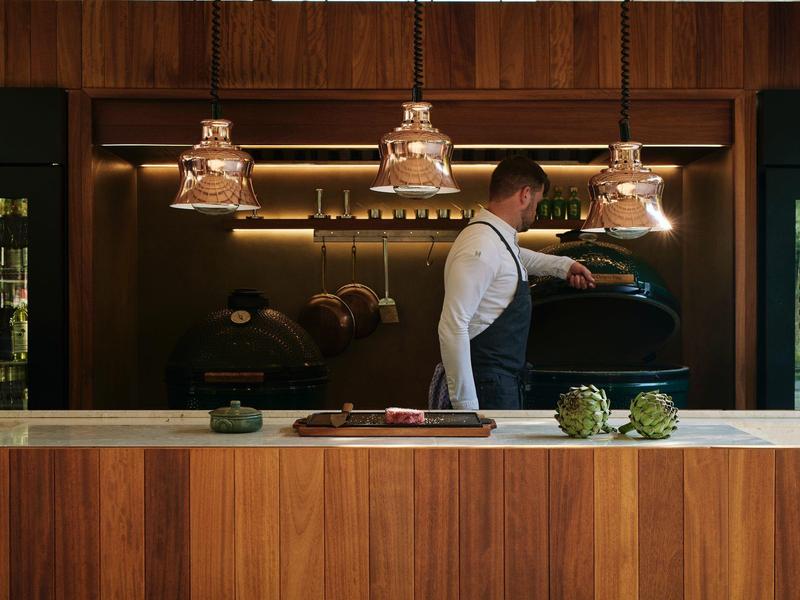 Mann in weißem Hemd und grauem Schürze arbeitet an einer Espressomaschine in einer modernen Bar.