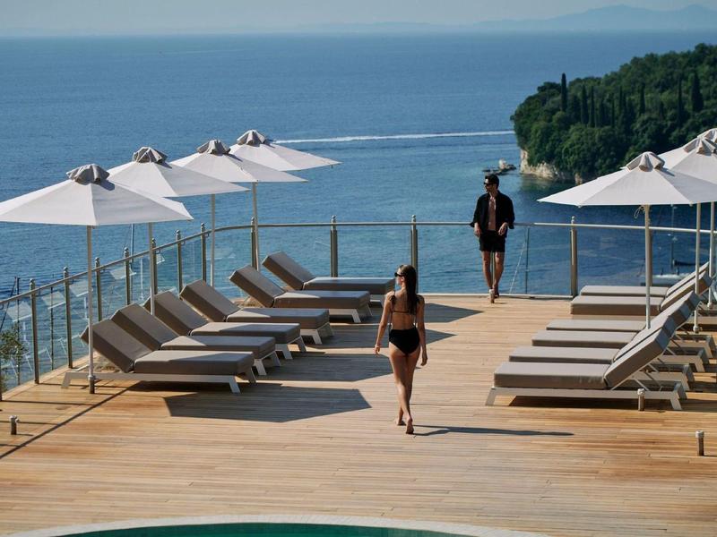 Sonnenliegen und Sonnenschirme auf einer Terrasse mit Meerblick und zwei Personen.