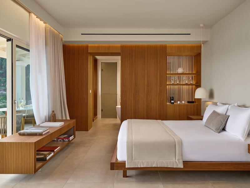 Helles Hotelzimmer mit großem Bett, Holzmöbeln und Blick auf grüne Natur.