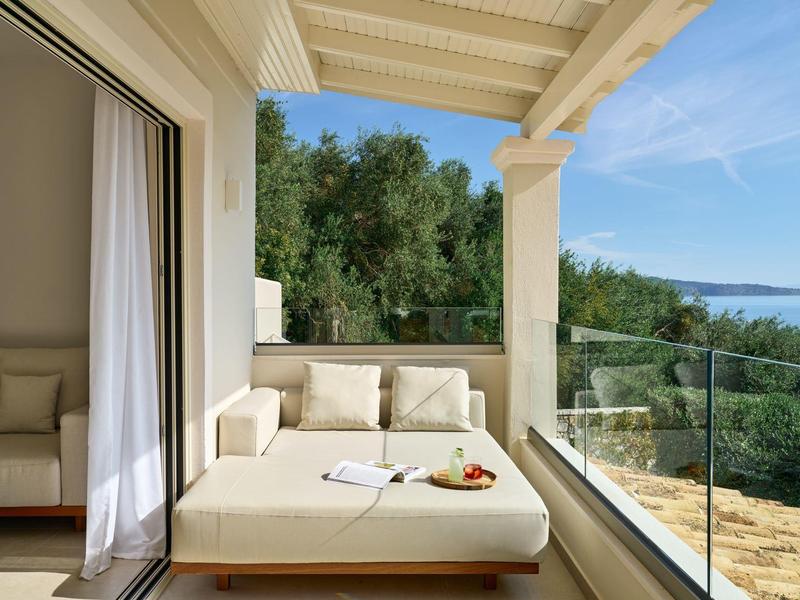 Balkon mit einem großen Liegesofa, Glasgeländer und Aussicht auf Grünflächen und Wasser.