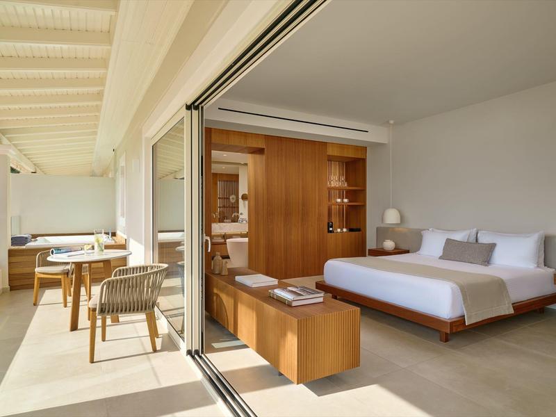 Moderner Hotelzimmerinnenraum mit großem Bett und Balkon mit Sitzbereich und Blick ins Grüne.