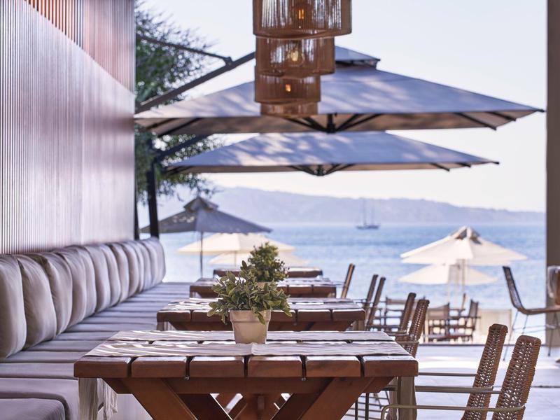 Terrassenrestaurant mit Holztischen, Pflanzen, Sitzbänken und Sonnenschirmen am Meer.