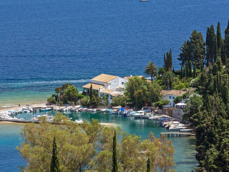 Kleiner Hafen mit Booten an der Küste, umgeben von grünen Bäumen und klarem blauem Wasser.