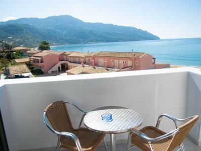 Balkon mit rundem Tisch und zwei Stühlen, Blick aufs Meer und Berge im Hintergrund.