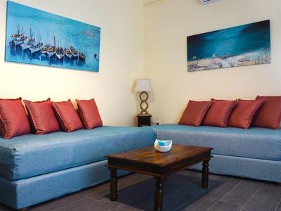 Wohnzimmer mit blauen Sofas, roten Kissen, Holztisch und maritimen Bildern an weißen Wänden.