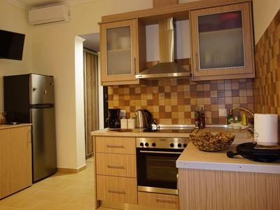 Kleine Küche mit Holzmöbeln, Edelstahl-Herd, Kühlschrank, Fernseher und braunem Fliesenspiegel.