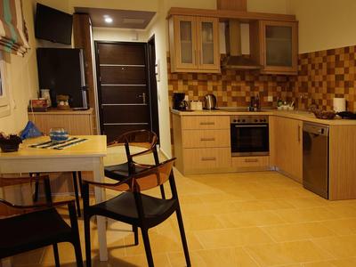 Helle Küche mit Holzmöbeln, braunen Fliesen, einem Tisch mit Stühlen und modernen Geräten.