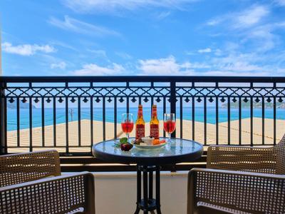 Balkon mit Tisch, Getränken und Snacks mit Blick auf das Meer unter blauem Himmel.