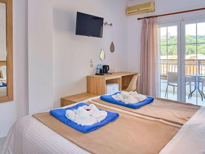 Helles Hotelzimmer mit zwei Einzelbetten, Balkon und Fernseher an der Wand.