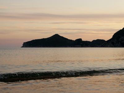 Sonnenuntergang am Strand mit Blick auf ruhiges Meer und Silhouette von Bergen.