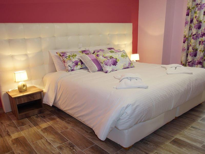 Ein großes Bett mit weißer Bettwäsche und Blumenmuster-Kissen steht vor roter Wand.