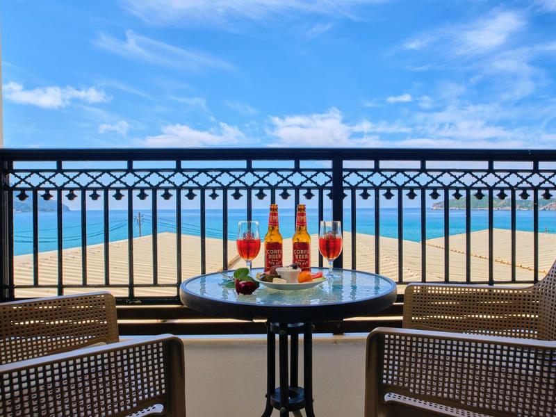 Balkon mit Tisch, Getränken und Snacks mit Blick auf das Meer unter blauem Himmel.