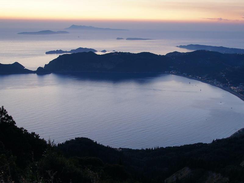 Bucht mit ruhigem Wasser und Bergen im Hintergrund bei Sonnenuntergang
