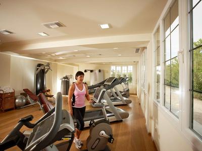 Žena cvičí na běžeckém pásu v světlé posilovně s velkými okny.