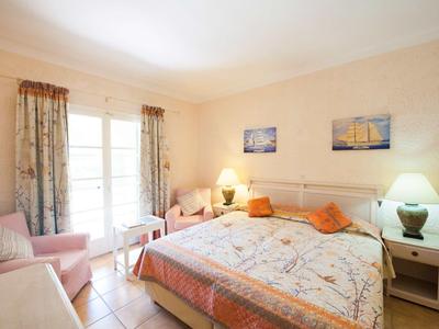 Hell eingerichtetes Schlafzimmer mit Doppelbett, Nachttischen, Lampen und einem Sessel am Fenster.