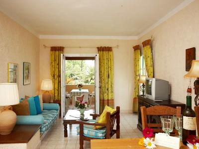 Helles Wohnzimmer mit gelben Vorhängen, blauen Sofas und Holz- und Glasmöbeln vor Balkon.