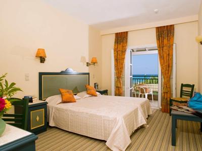 Hell eingerichtetes Hotelzimmer mit zwei Betten, Balkon und Blick auf das Meer.