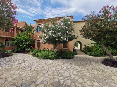 Hotelové nádvoří s kamennou dlažbou, stromy a středomořskou architekturou pod částečně oblačnou oblohou