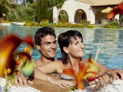 Pár odpočívá u hotelového bazénu s rostlinami v popředí