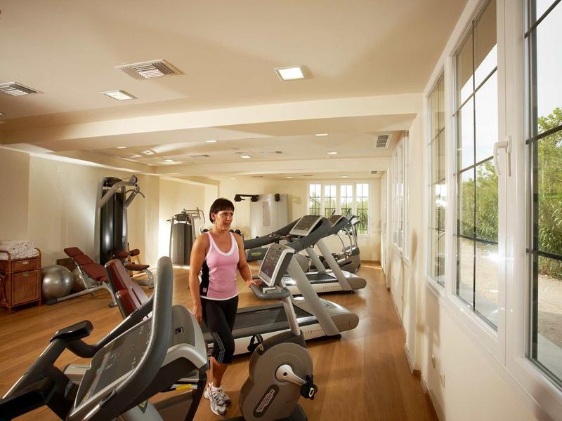 Frau trainiert auf Laufband in hellem Fitnessraum mit großen Fenstern und Holzboden.