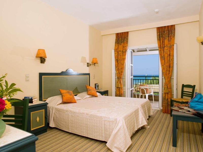 Hell eingerichtetes Hotelzimmer mit zwei Betten, Balkon und Blick auf das Meer.